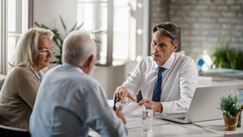 Mid adult insurance agent with mature couple analyzing financial reports and communicating during the meeting in the office.